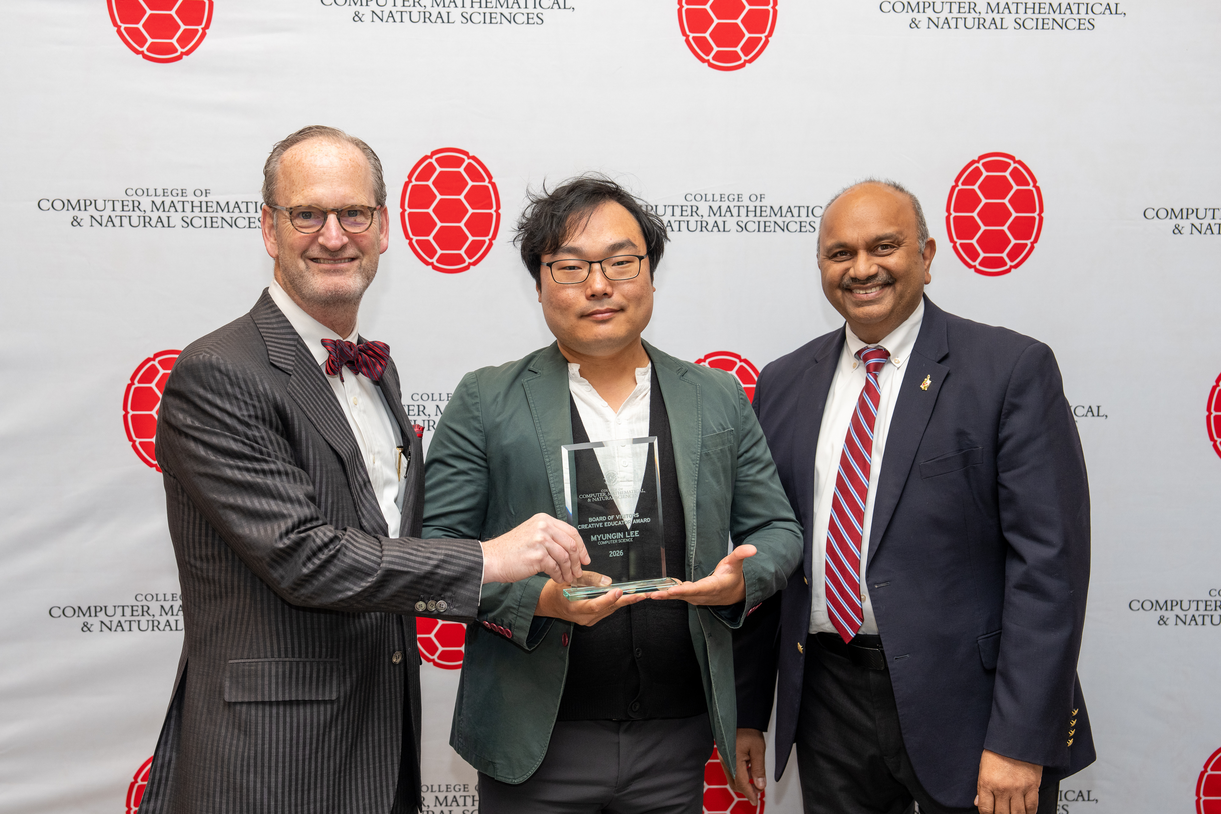 Three people holding an award in front of a step-and-repeat banner