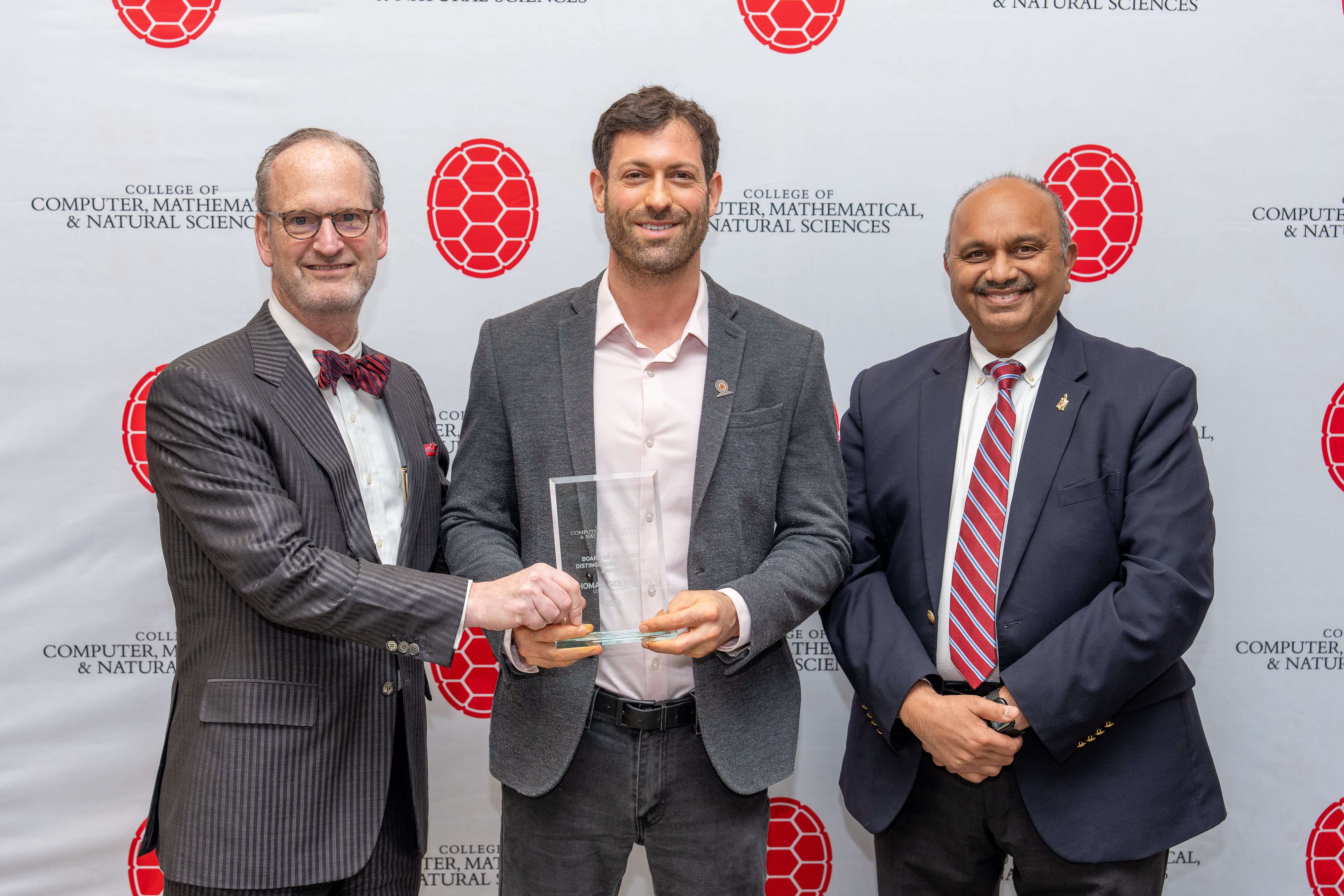 Three people holding an award in front of a step-and-repeat banner