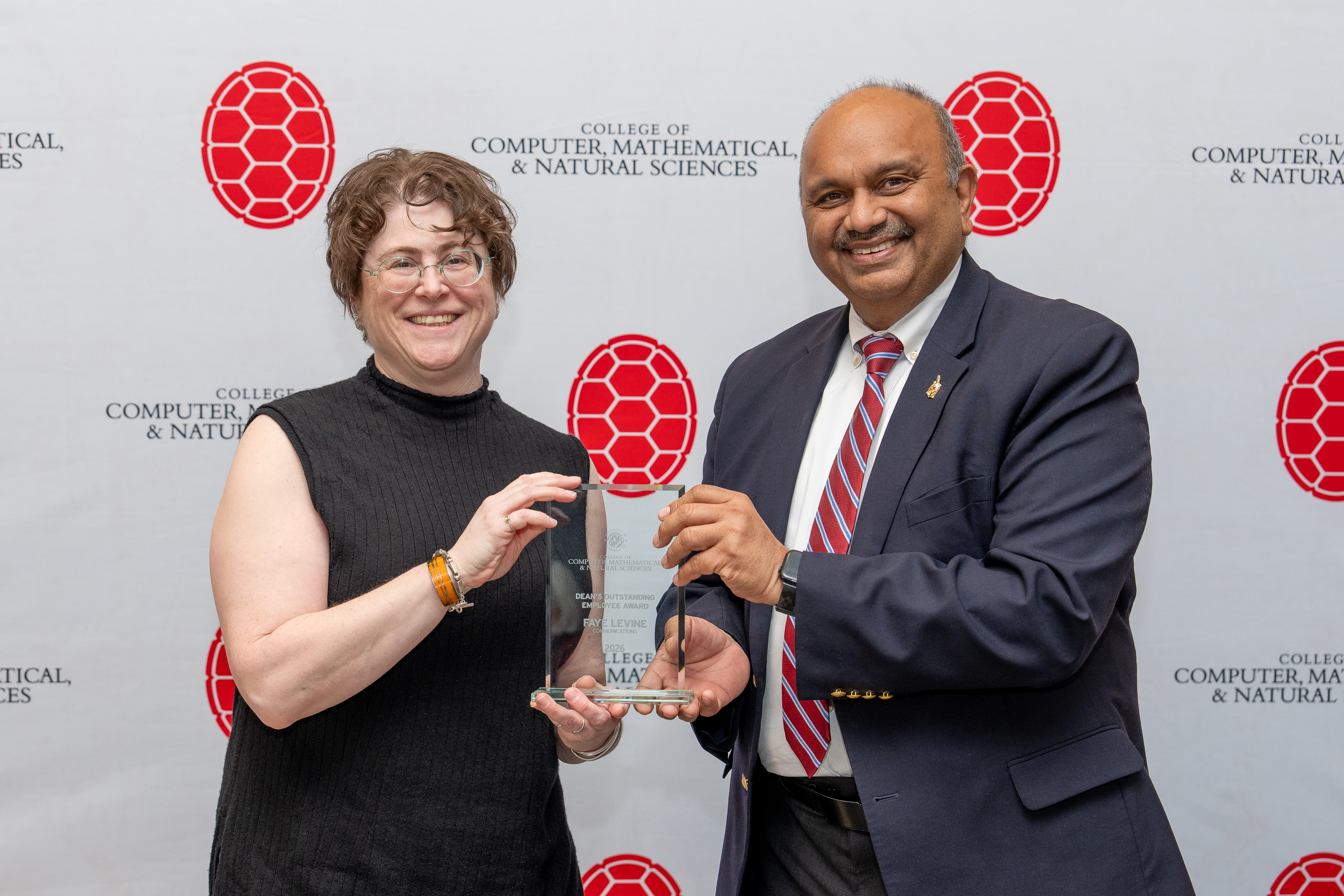 Two people holding an award in front of a step-and-repeat banner
