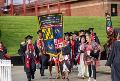 A group of graduates wearing regalia carrying gonfalon into commencement