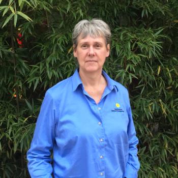 Sara Gallager in a blue Smithsonian shirt poses in front of bamboo.