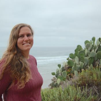Jessica Goodheart standing on a beach by the water among cactus plants.